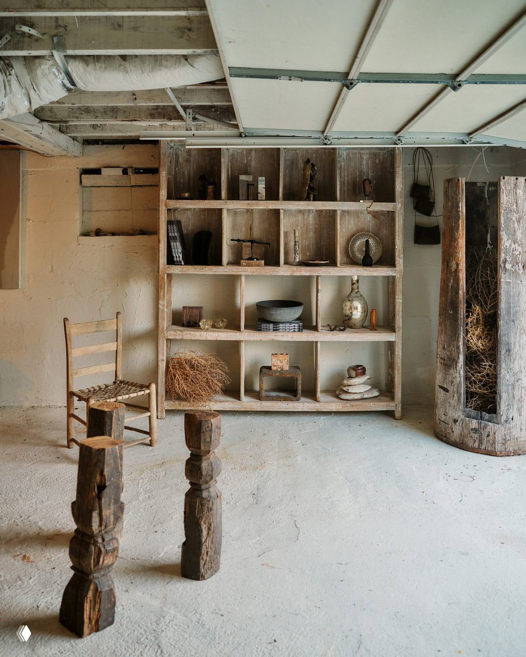 Стеллаж с разделёнными секциями, наполненный деревянными и керамическими предметами, коллаж антикварных деталей в подсобном пространстве дома.