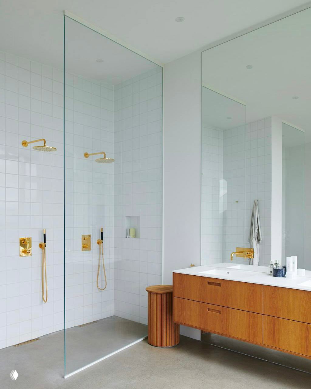 Светлая ванная комната с двумя душевыми кабинами, большой зеркальной стеной и деревянной тумбой — лаконичный минимализм в сочетании с золотыми акцентами смесителей.