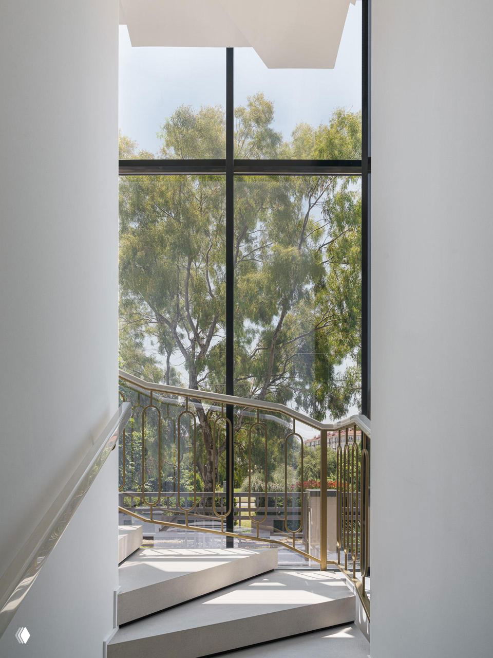 Интерьер лестничного холла с широкими ступенями, декоративным поручнем и большим окном, в котором отражается зелень сада за домом.