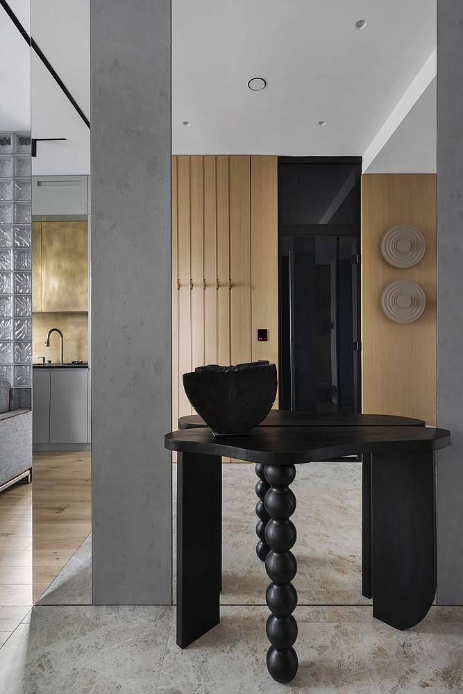 Прихожая с декоративным столом на фоне вертикальных деревянных панелей и зеркала, сочетание серого бетона и тёплого дерева в компактном пространстве.