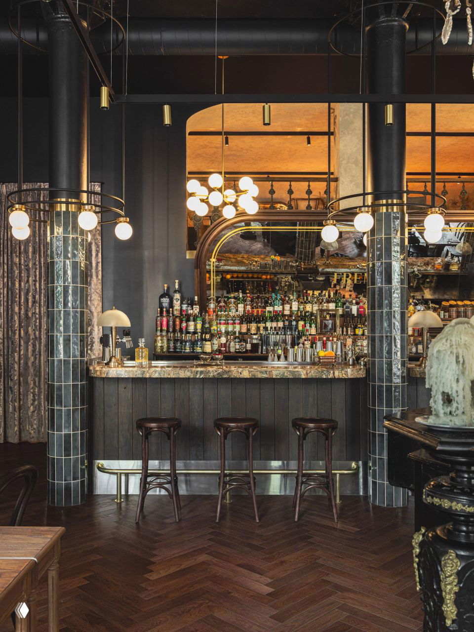 Барная зона с зеркальной стеной, облицованными плиткой колоннами, полированной барной стойкой и латунными акцентами в оформлении.