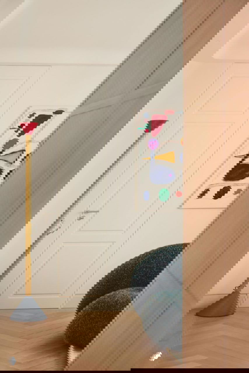 Узкий ракурс прихожей: высокая дверь, яркая напольная лампа и абстрактная картина как цветовой акцент на фоне светлых стен.