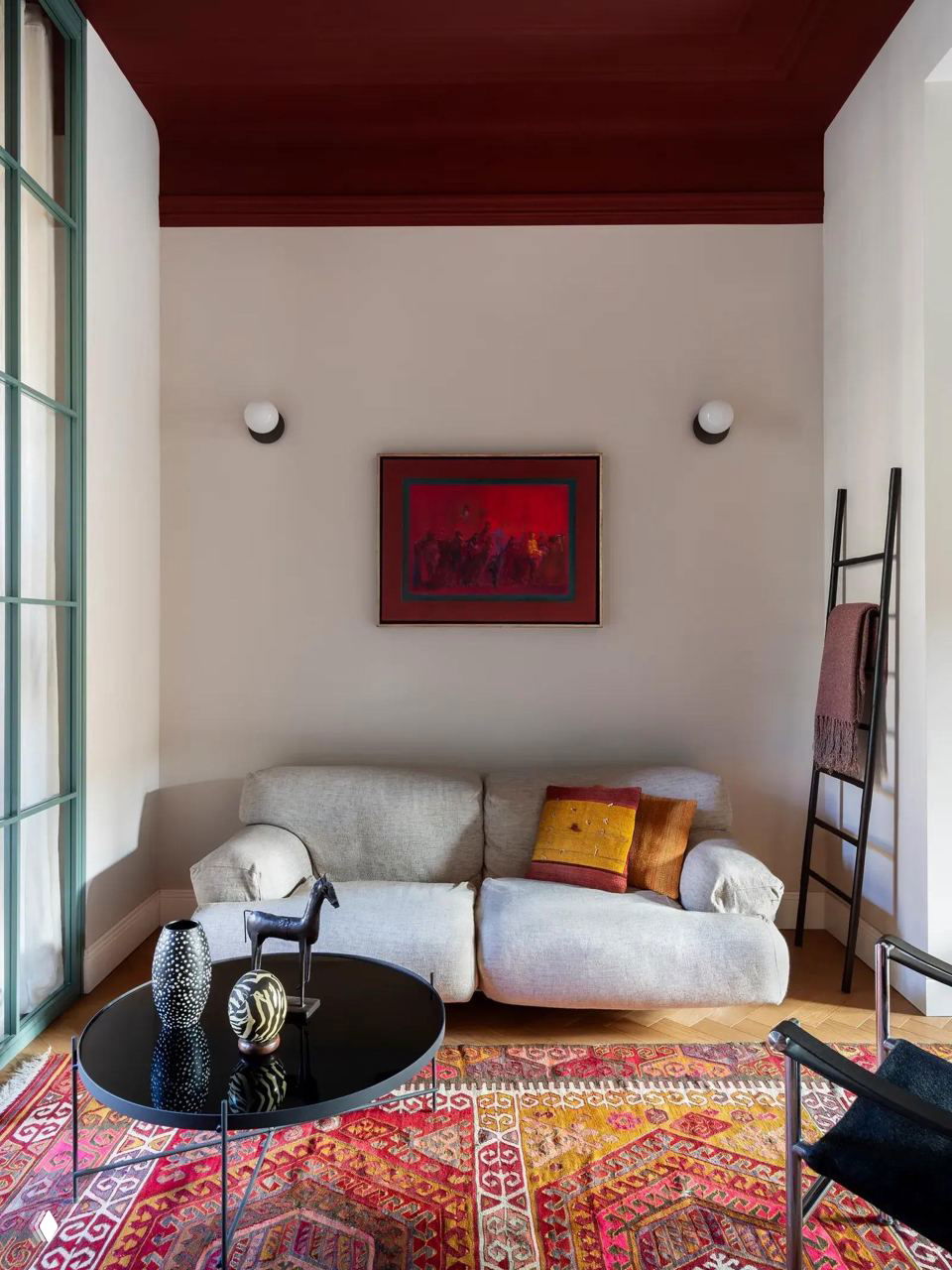 Уютный небольшой диван в нише с ярким восточным ковром и красными акцентами в потолке и текстиле — контрастные цвета в компактном пространстве.