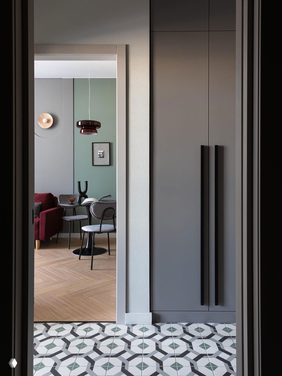 Вид через дверной проём: столовая зона и прихожая с графичным узором на плитке, монохромными шкафами и аккуратным переходом материалов пола.