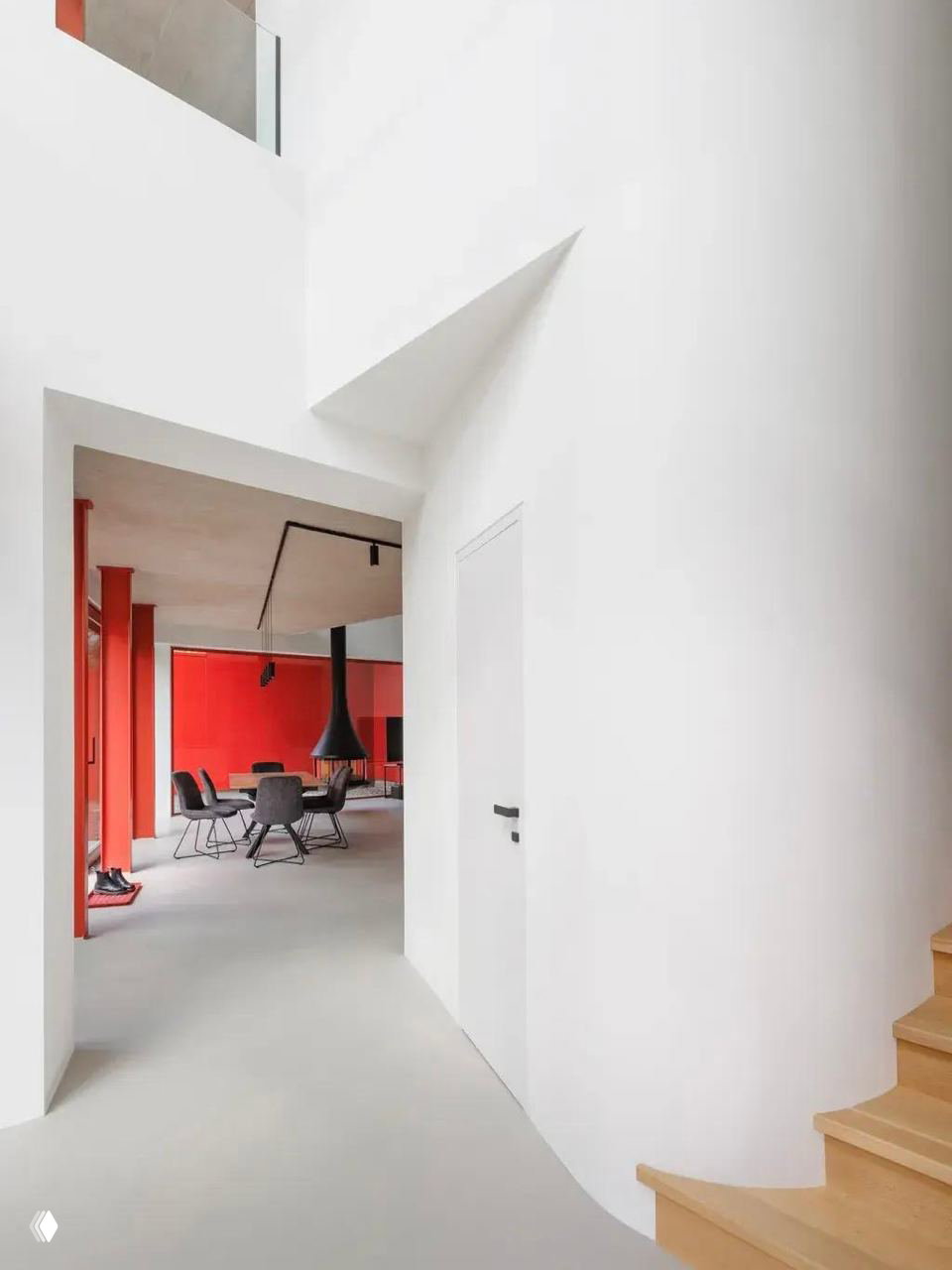 Белый холл и лестница внутри дома, вид на красную фонную стену гостиной: сочетание чистых белых поверхностей, деревянной лестницы и ярких красных акцентов.
