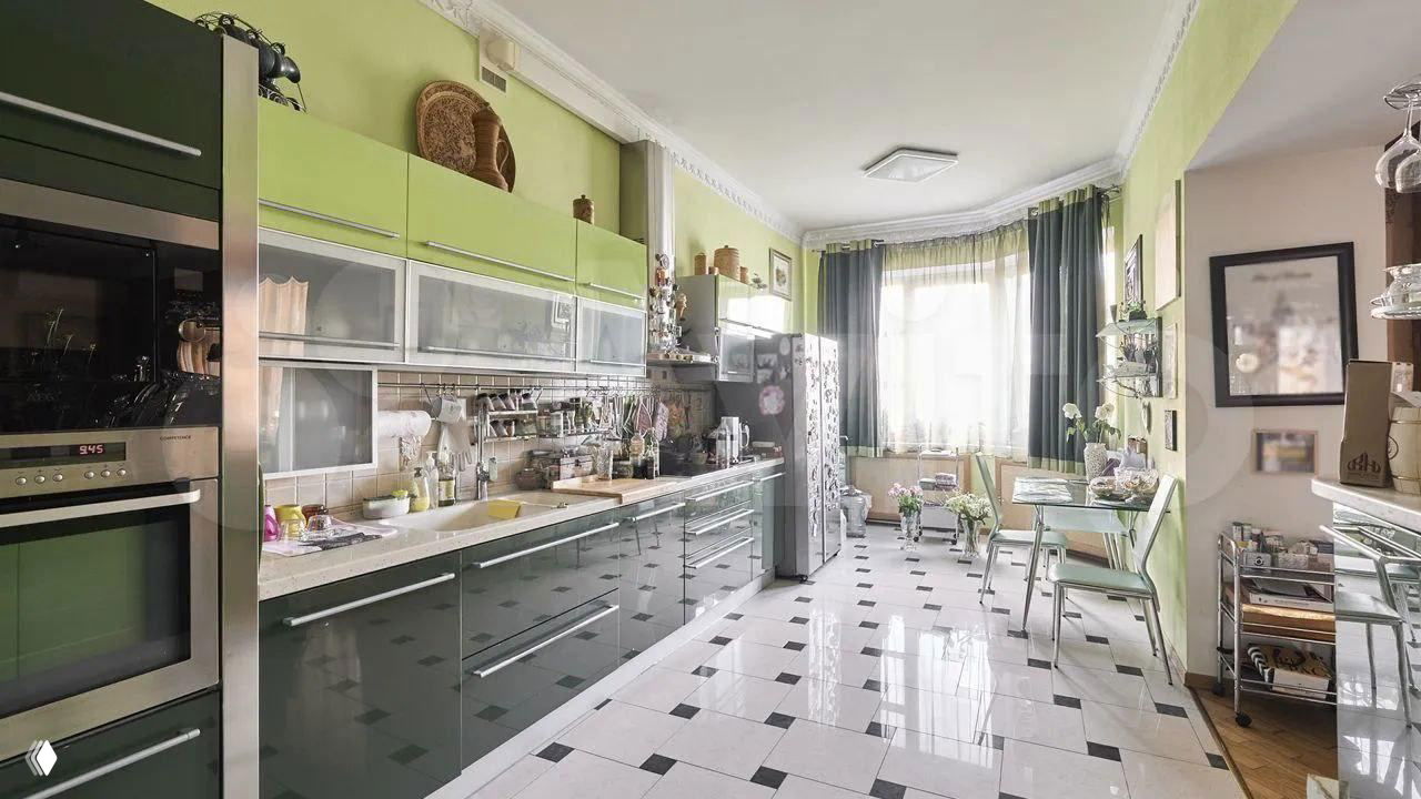 Современная кухня зелёного оттенка с глянцевыми фасадами, бытовой техникой и контрастной чёрно-белой плиткой на полу — заметный контраст с классическим интерьером остальной квартиры.