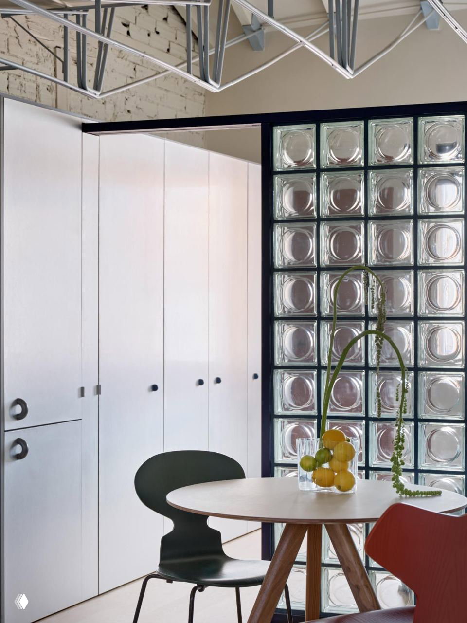 Обеденная зона с круглыми стеклянными блоками в перегородке, деревянным столом и стульями; сочетание стекла, керамики и стального каркаса интерьера.