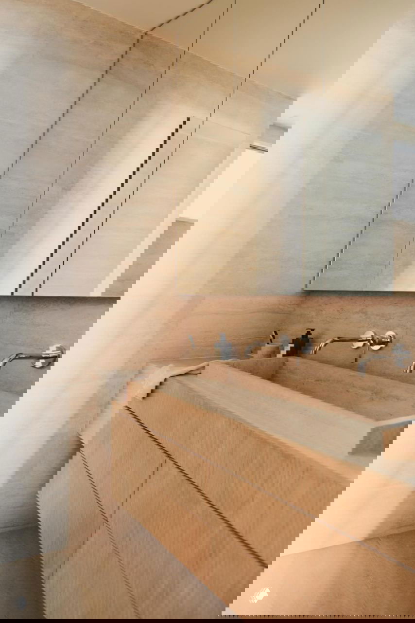 Ванная комната с мраморной отделкой и деревянной тумбой-умывальником в натуральных бежевых тонах и зеркалом в нише.