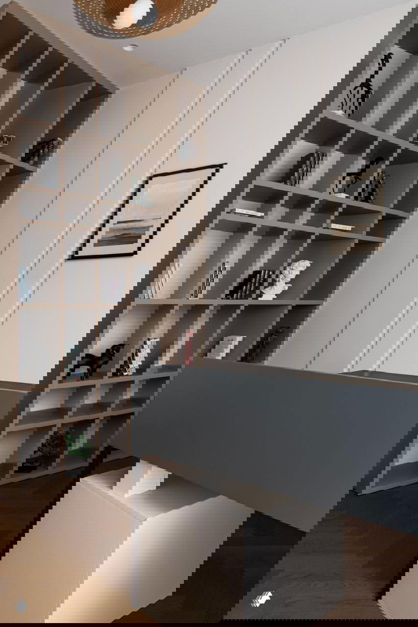 Рабочая зона и открытые кубические полки в нейтральных тонах; вид на письменный стол и декоративные объекты на стеллаже в коридоре.