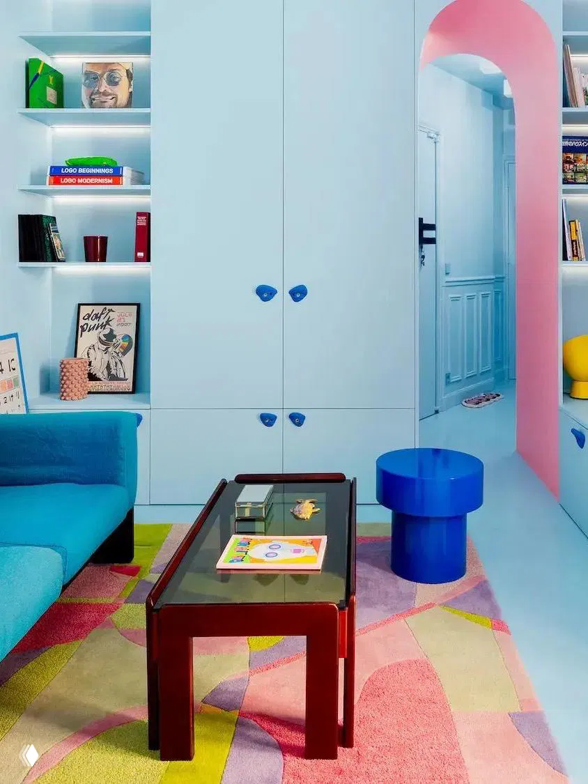 Яркая игровая комната с голубыми шкафами, синим диваном и разноцветным ковром — использование насыщенных тонов для ощущения простора и настроения.