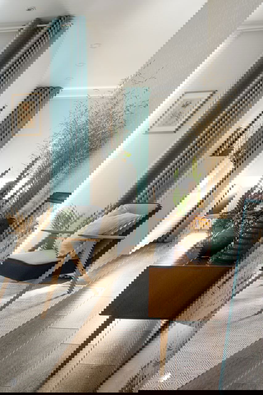 Узкий проход между прихожей и гостиной: консоль из дерева, вазы и декор, на полу плитка под дерево и лёгкое наполнение пространства растениями.