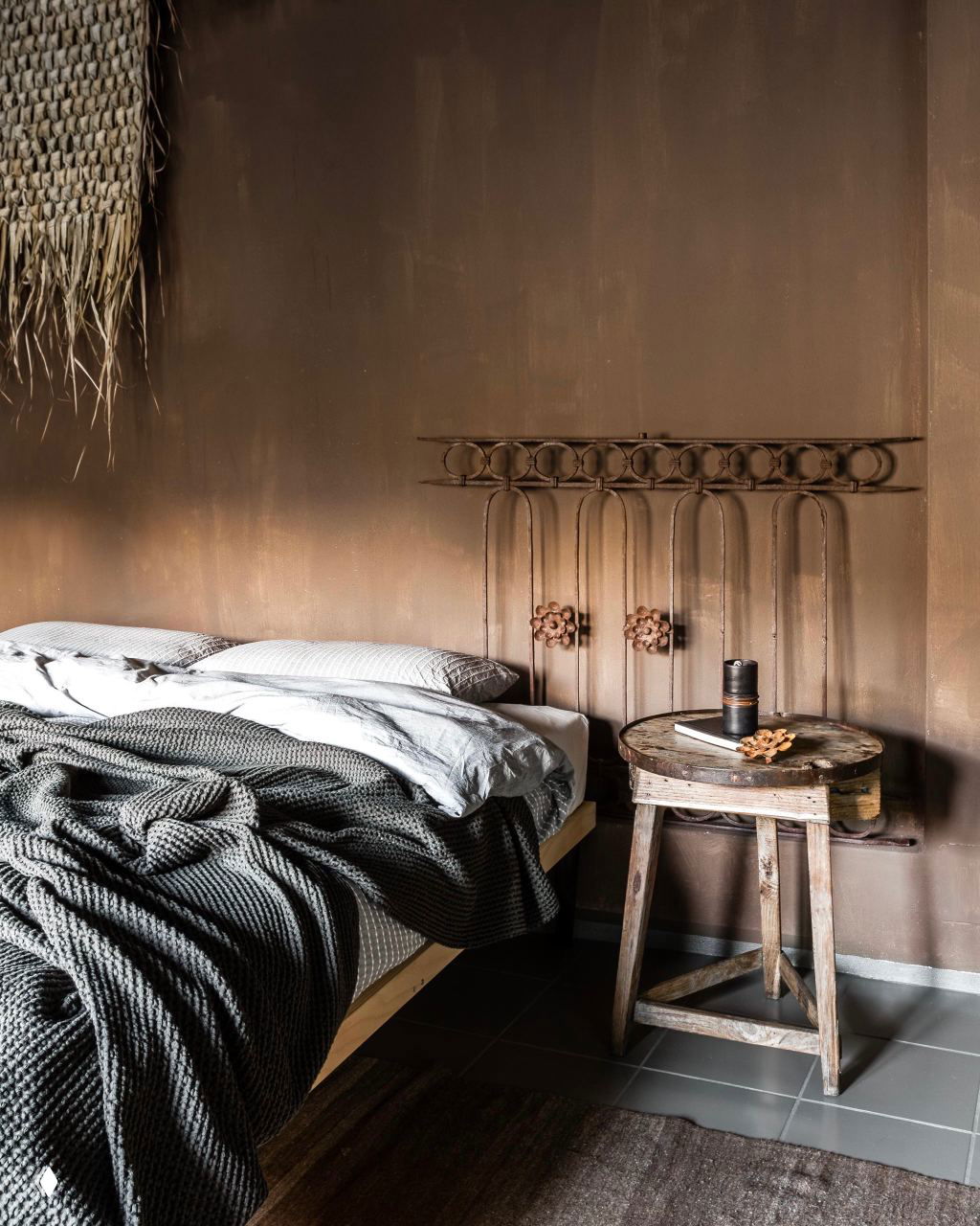 Спальня с коричневыми стенами и винтажной металлической спинкой кровати; текстуры и тёплые оттенки коричневого формируют уютную камерную обстановку.