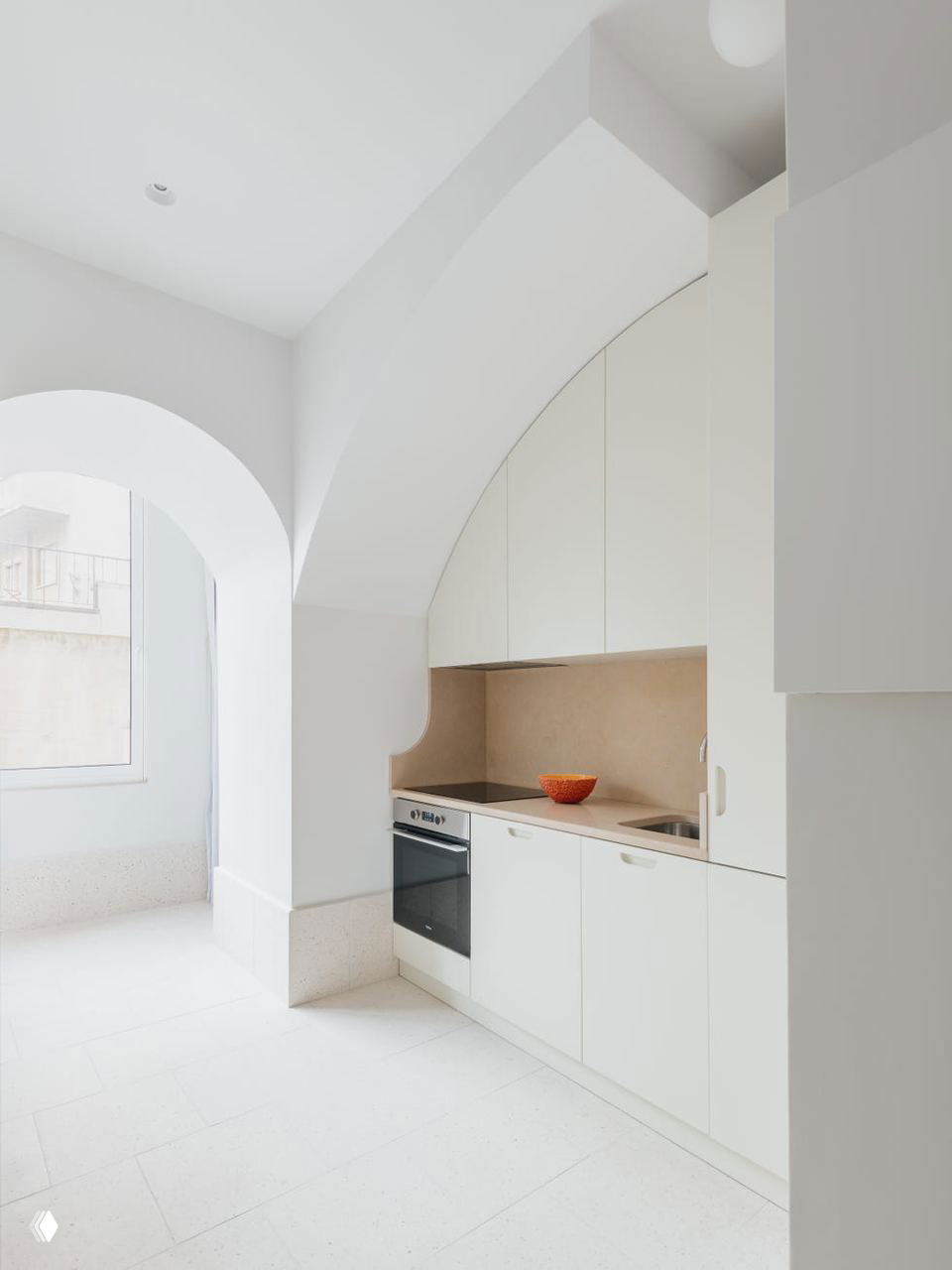 Кухонный угол с арочной нишей: светлая мебель цвета слоновой кости, компактная столовая зона и плавные линии, объединяющие кухню с остальным пространством.