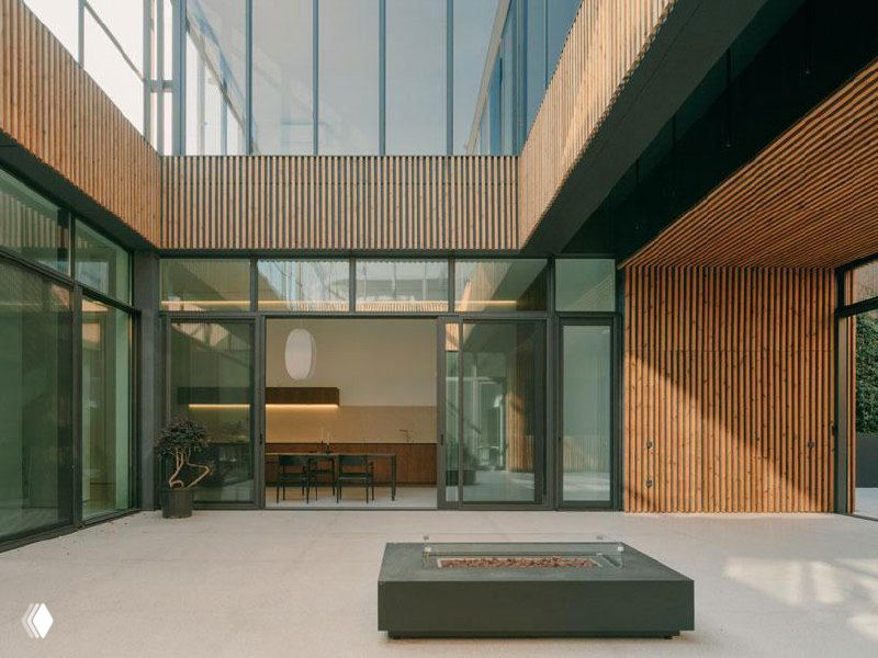 Вид внутреннего двора и остеклённой зоны под нависающими объёмами: прозрачные фасады, связь между уровнями и дневной свет, проникающий в центр плана.