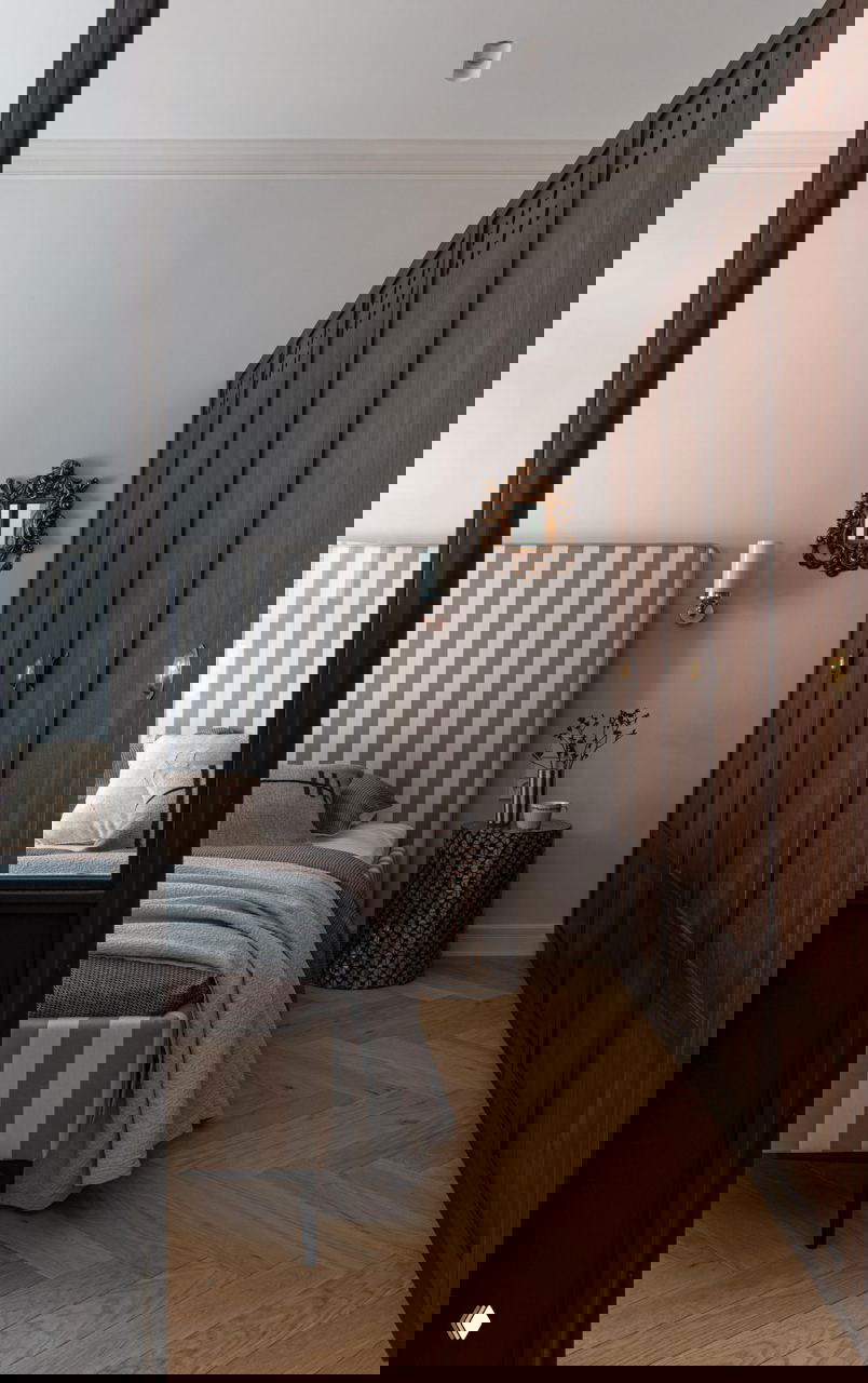 Спальная зона с полосатым изголовьем кровати, высокими деревянными шкафами и небольшим резным венецианским зеркалом на стене у кровати.