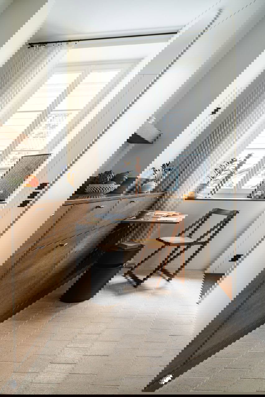 Рабочее место у окна в маленькой квартире: складной стол, простой деревянный стул и светлый текстиль на фоне большого окна.