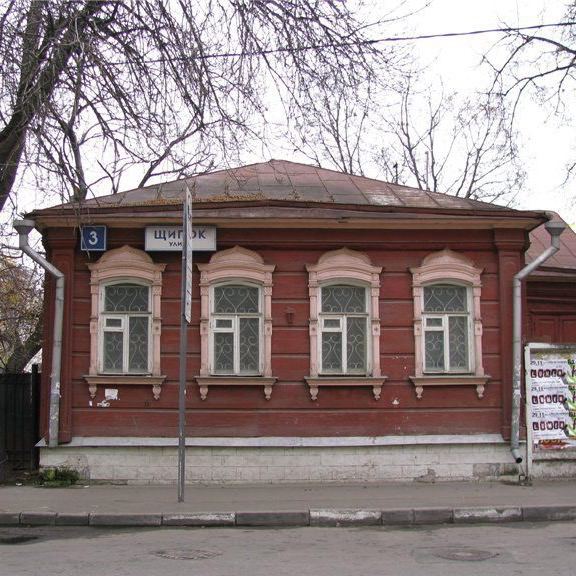 Невысокий деревянный дом в традиционном стиле с табличкой «Щипок» на углу; фасад, деревянные наличники и городской тротуар на переднем плане.