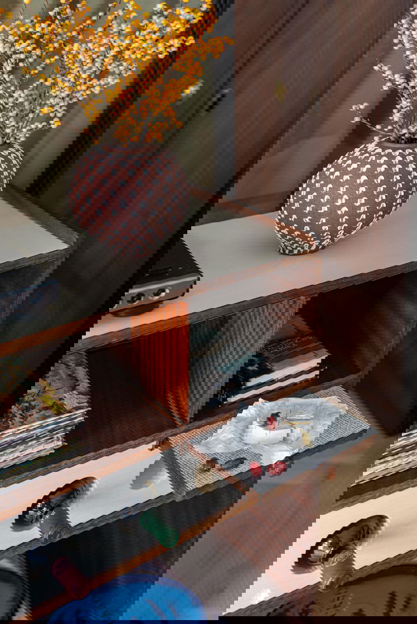 Крупный план винтажного барного шкафа с отделениями для бутылок, журналами, выдвижной подставкой и предметами декора в тёплой древесной отделке.