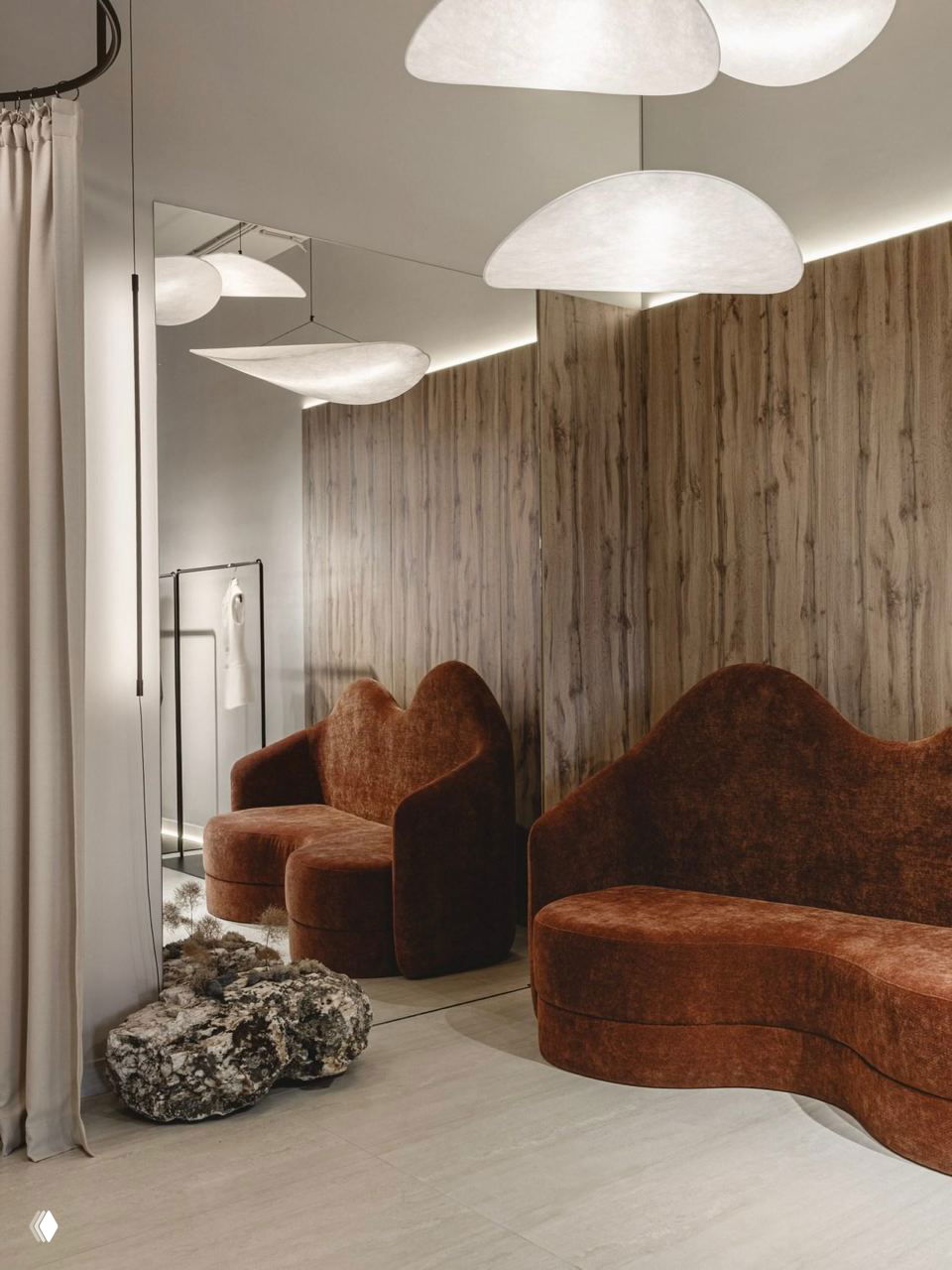 Примерочная зона с деревянной фактурой на стене, мягкие коричневые волнообразные диваны и природный камень на полу как композиционный элемент интерьера.