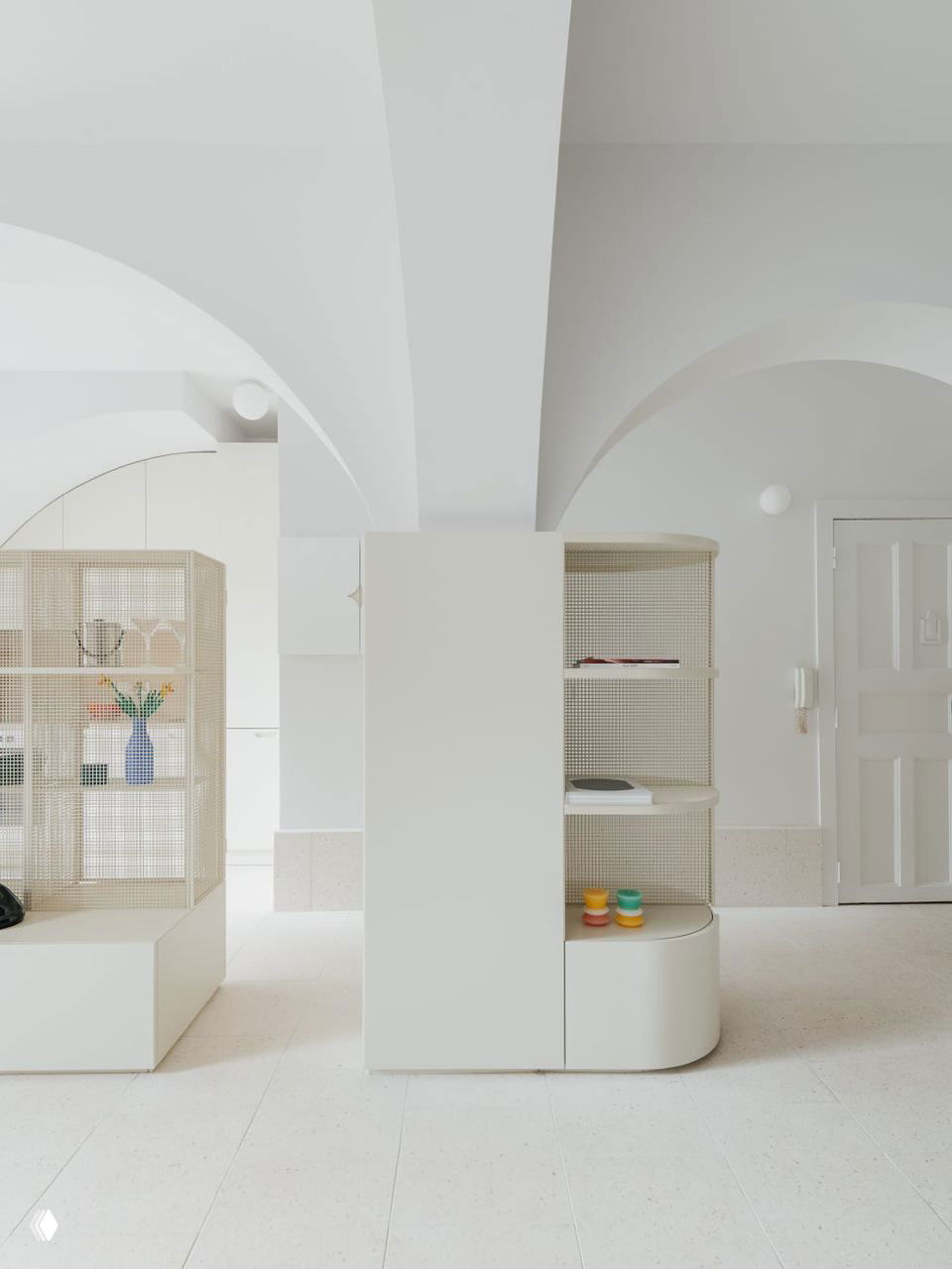 Перспектива коридорной части студии с арками и низкими шкафами; строгие светлые поверхности и аккуратные закругленные углы мебели, создающие целостность пространства.