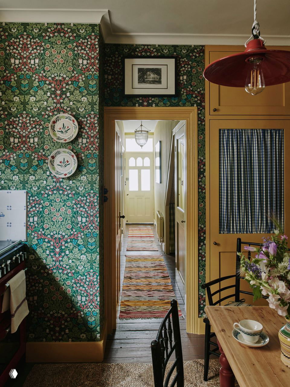 Вид через дверной проём на длинный холл с ковровыми дорожками; фрагменты кухни и дверей подчёркивают компактную планировку и связь зон в доме.