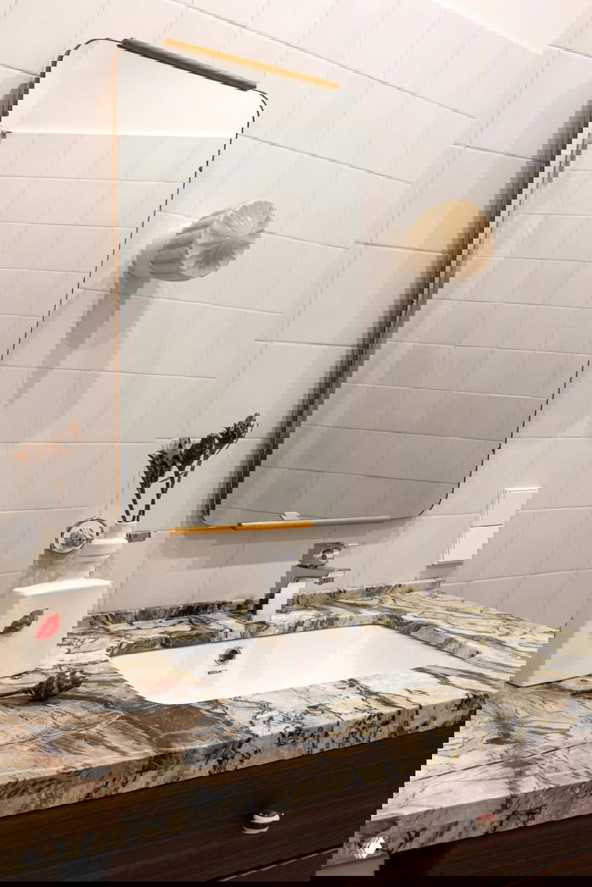 Ванная комната с мраморной столешницей, прямоугольной встроенной раковиной и настенным зеркалом в тонкой деревянной оправе.