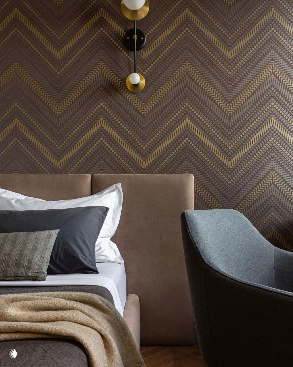 Спальня с мягким коричневым изголовьем и декоративными обоями с геометрическим узором; спокойная палитра и текстиль создают уют и глубину интерьера.