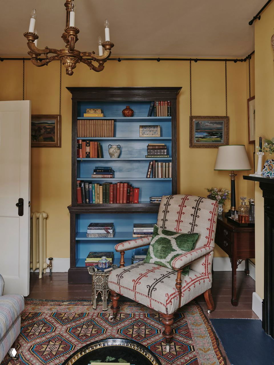 Ниша с книжным шкафом, окрашенным в голубой тон, рядом антикварное кресло и небольшой столик — сочетание практичности и декоративных акцентов в гостиной.