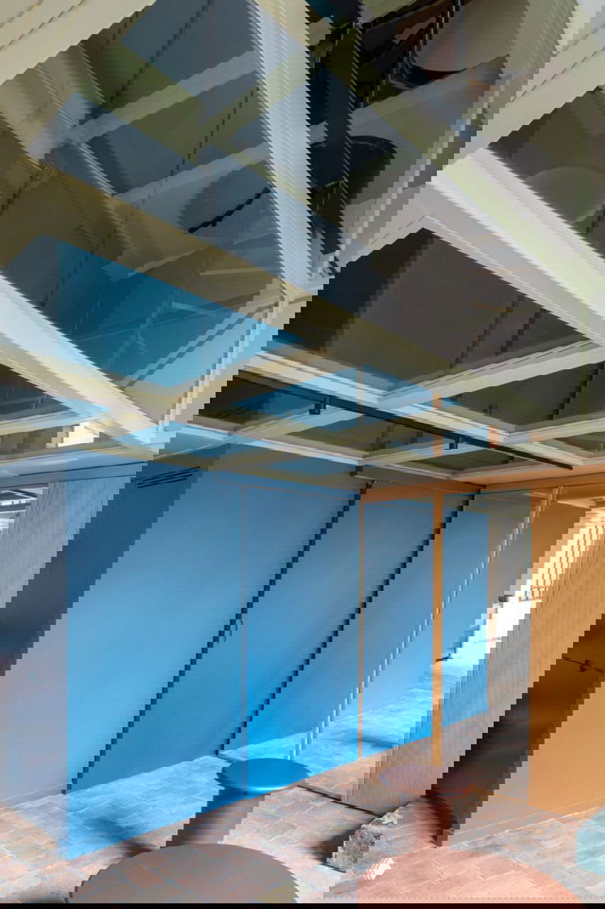 Синий объём кухни‑ниши и стеклянный потолок над проходом: зеркальные панели усиливают ощущение высоты и глубины пространства.