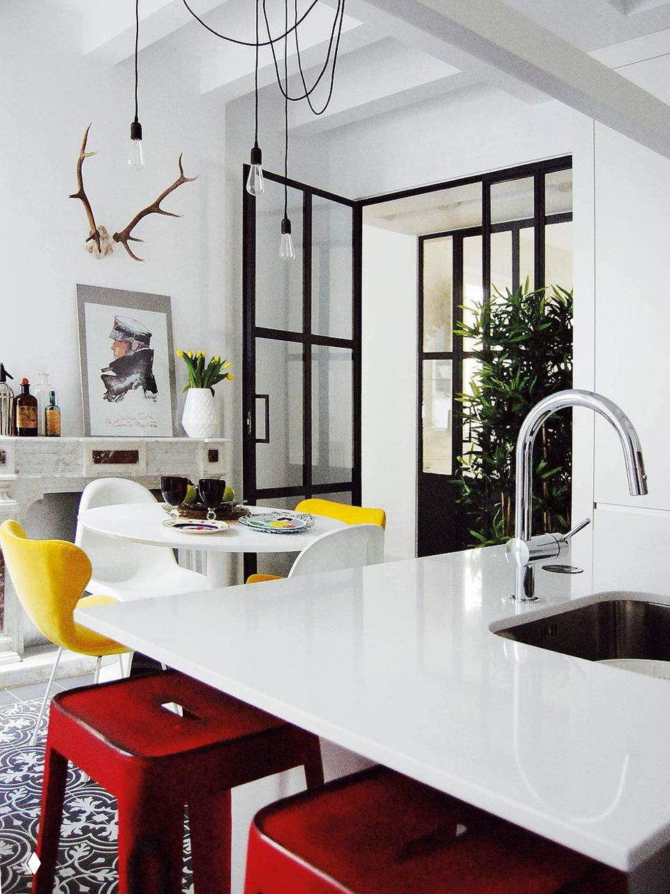 Кухонный вид с белой рабочей поверхностью и красными барными табуретами, на фоне виден камин в классическом стиле и чёрно‑стеклянная дверь.