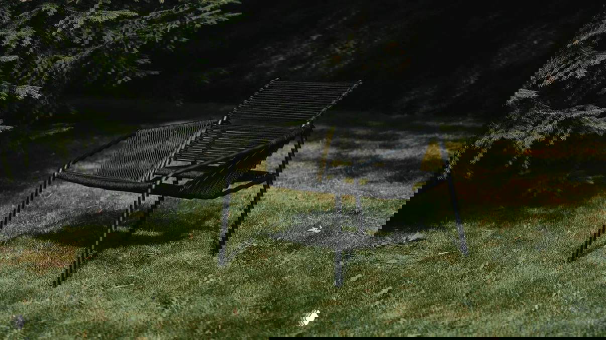 Чёрное уличное кресло с минималистичным силуэтом стоит на газоне рядом с елью, демонстрация дизайна кресла для сада и террасы.