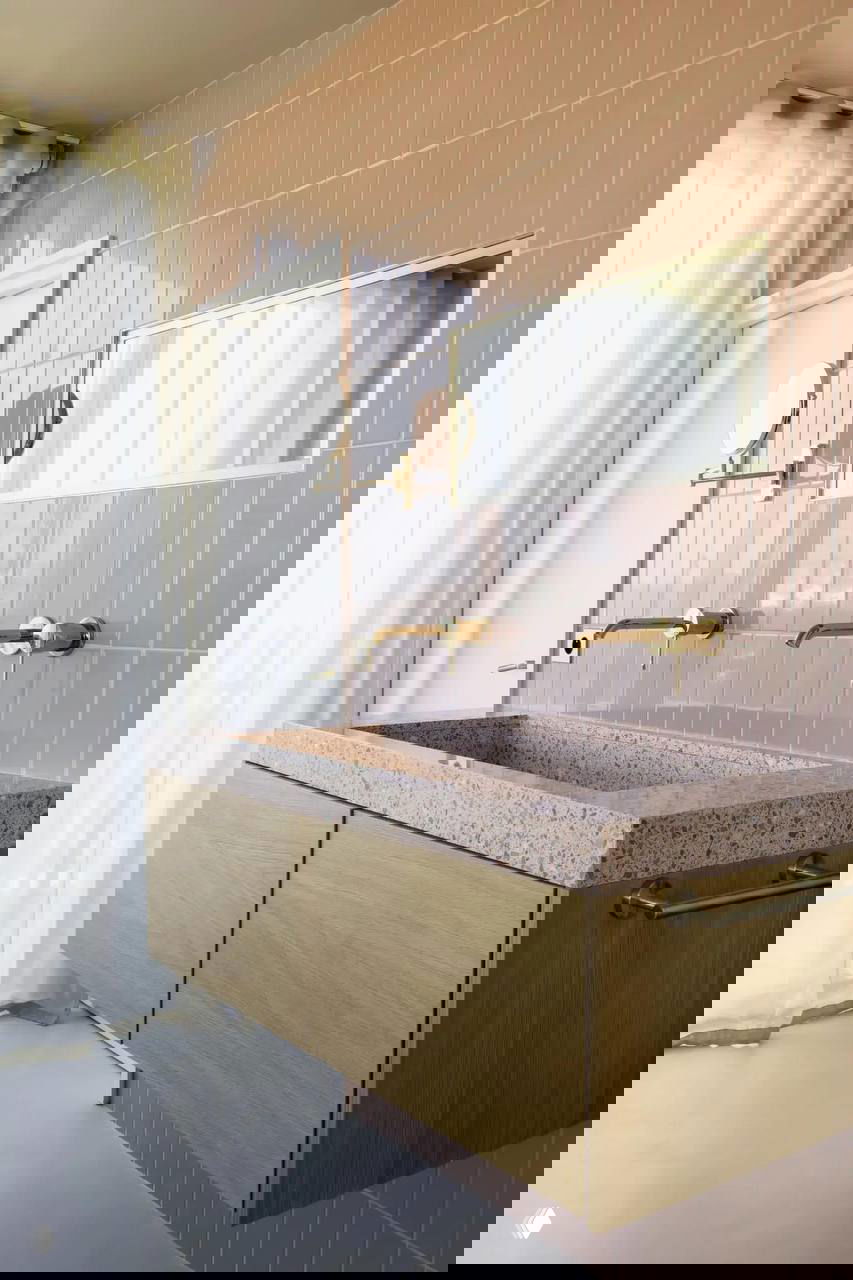 Ванная комната с розовой плиткой: подвесная тумба из светлого дерева и интегрированная раковина из терраццо под большим зеркалом.