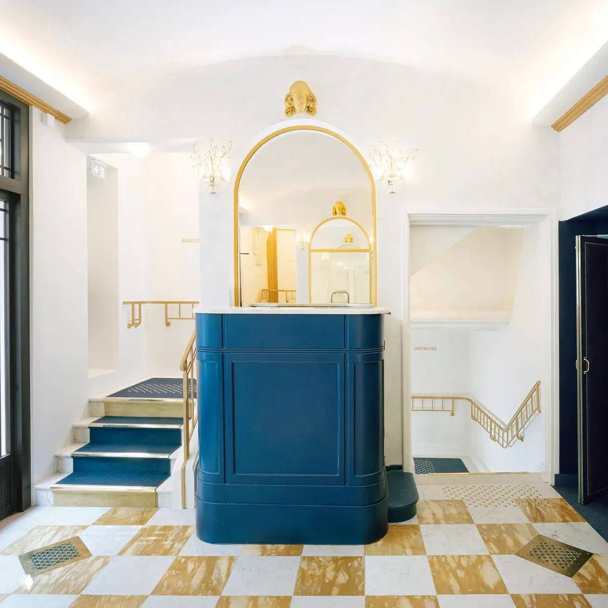 Ресепшн и вход в театре Дауну: синий приёмный стол, мраморный шахматный пол и золочёные зеркальные рамы — сочетание белого, золота и синего в ар-деко интерьере.