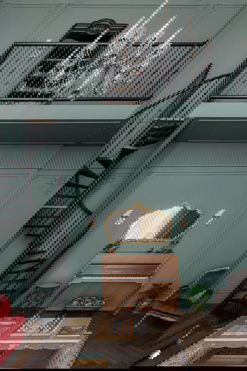 Двухуровневая зона с антресолью-библиотекой, чёрной винтовой лестницей и крупной хрустальной люстрой на фоне глубокого зелёного тона стен.