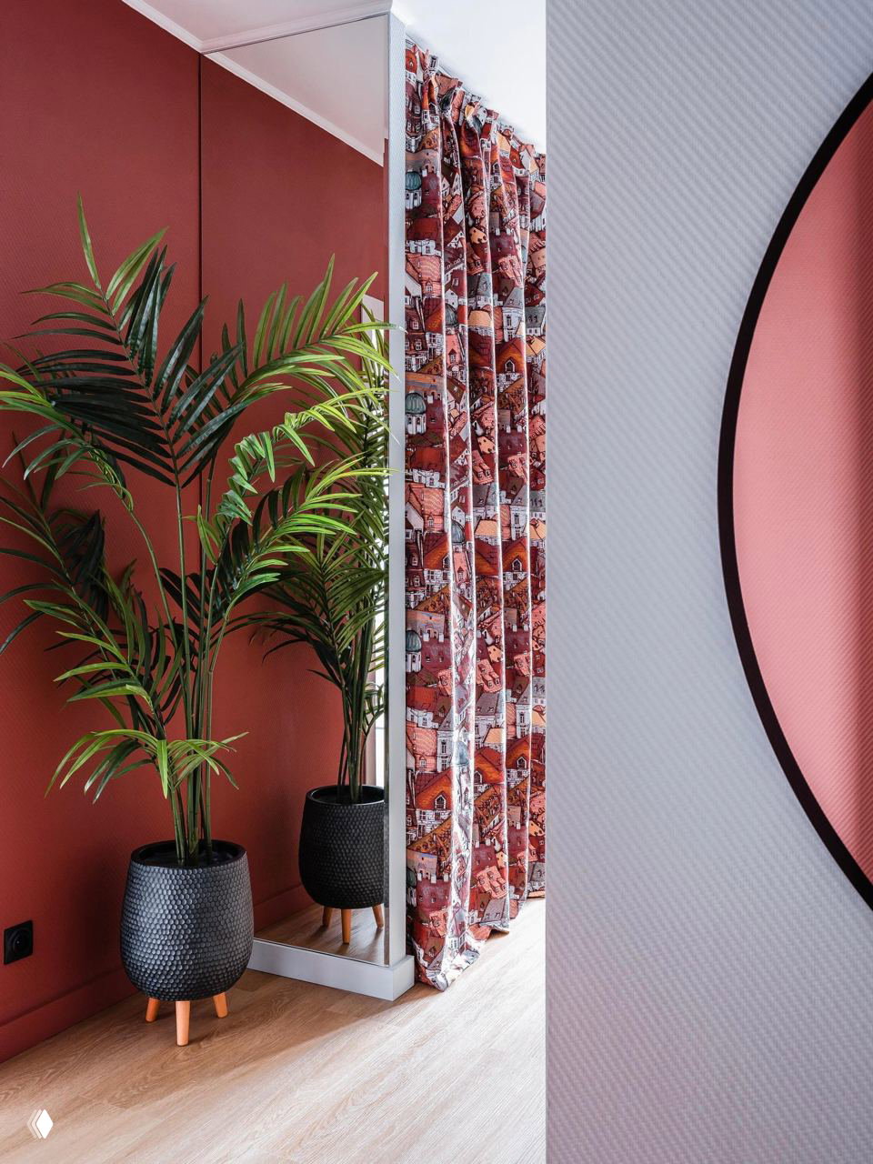 Угол с бордовыми стенами: зеркальная панель, высокие комнатные растения в тёмных горшках, узорчатые бордовые шторы и светлый ламинатный пол
