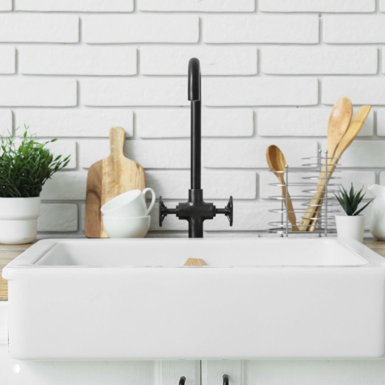 Крупный план кухонной мойки и крана на фоне белой кирпичной плитки: деревянные доски и маленькие горшки с растениями создают домашнюю атмосферу.
