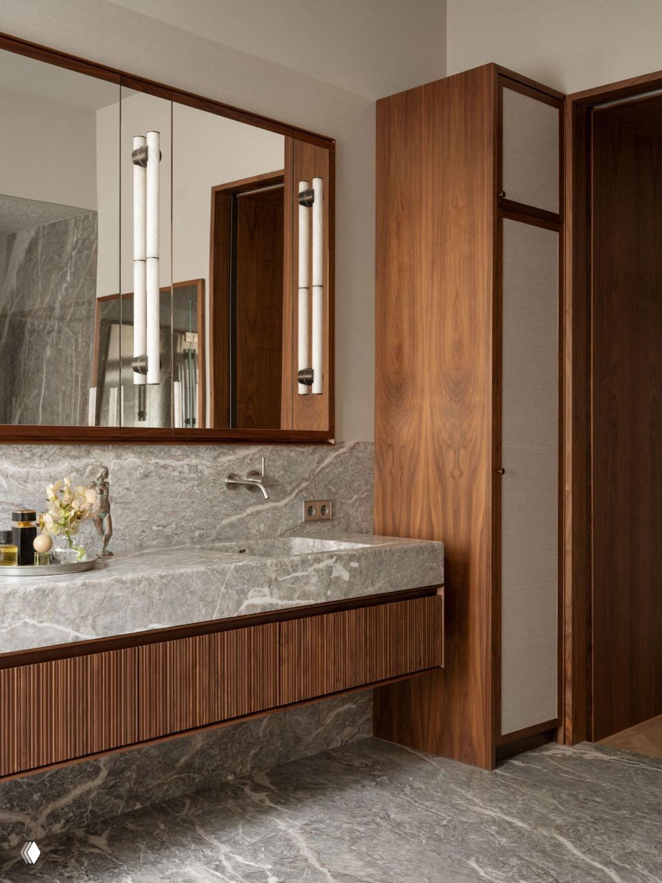 Ванная комната с широкой столешницей и подвесной тумбой из тёмного ореха, выполненные из однородного серого итальянского мрамора, с врезным смесителем в стене.