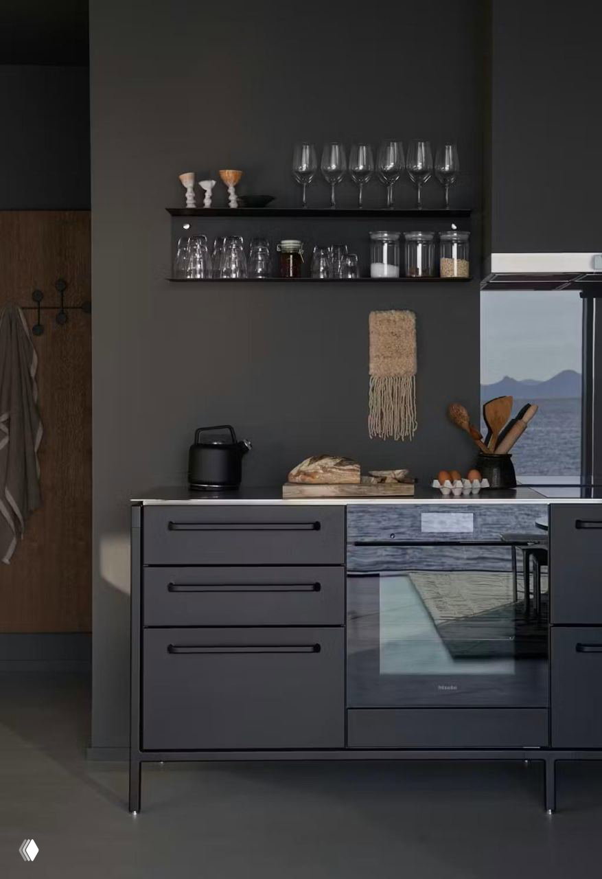 Кухонный уголок в тёмных натуральных тонах: минималистичные фасады, открытые полки с посудой и окно с видом на морской горизонт.
