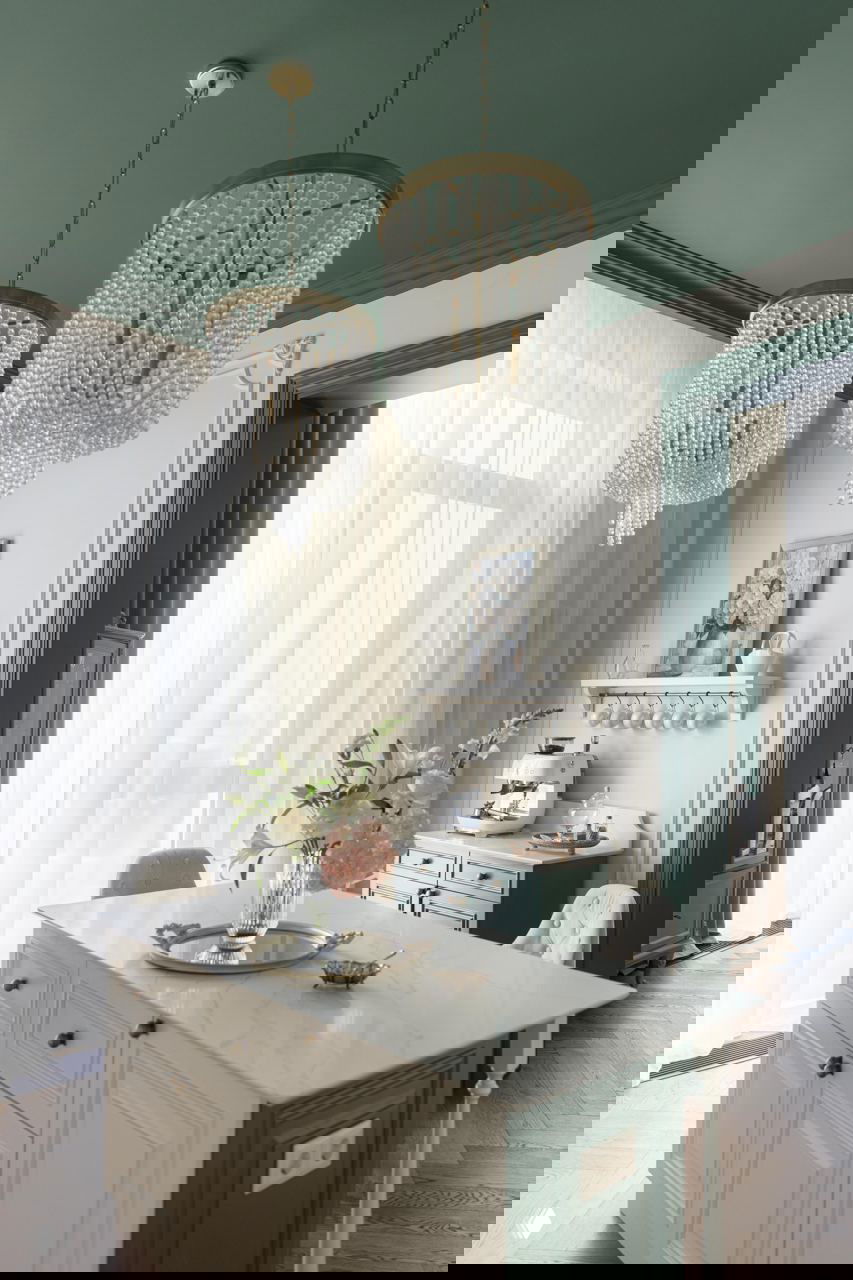 Кухонная зона с островом и двумя подвесными светильниками из стеклянных бусин, большие оконные шторы и пастельные декоры в классическом ключе.