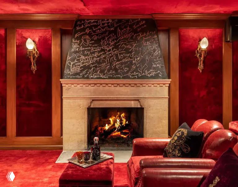 Интерьерный снимок гостиной особняка: уютная красная комната с каминным порталом, кожаными креслами и низким столиком у камина.
