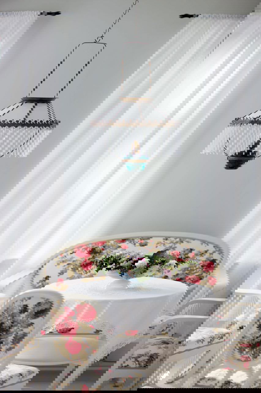 Интерьерный уголок с круглым столом и стульями в цветочный принт, мягким диваном и подвесной люстрой — винтажная, уютная композиция в светлых тонах.