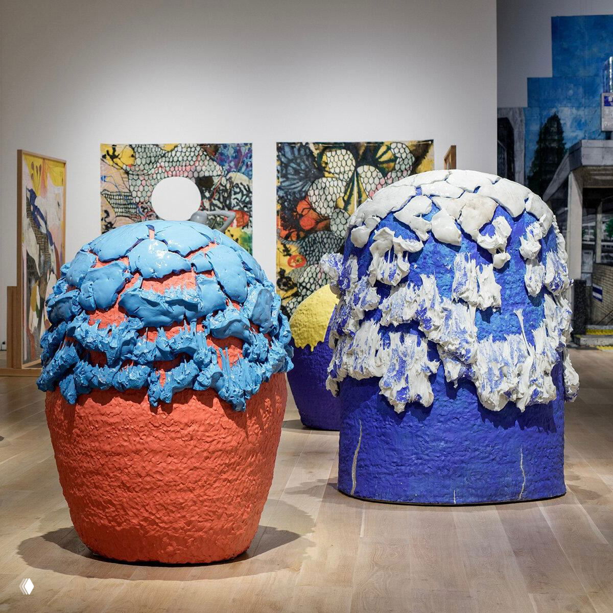Крупные текстурные скульптуры в выставочном зале: округлые формы с яркой сине‑белой и красной пастой на переднем плане, галерейная экспозиция.