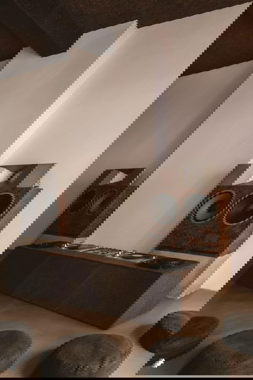 Зона прослушивания с массивными деревянными колонками, низкой консолью и проигрывателями винила, оформленная в теплых естественных тонах.