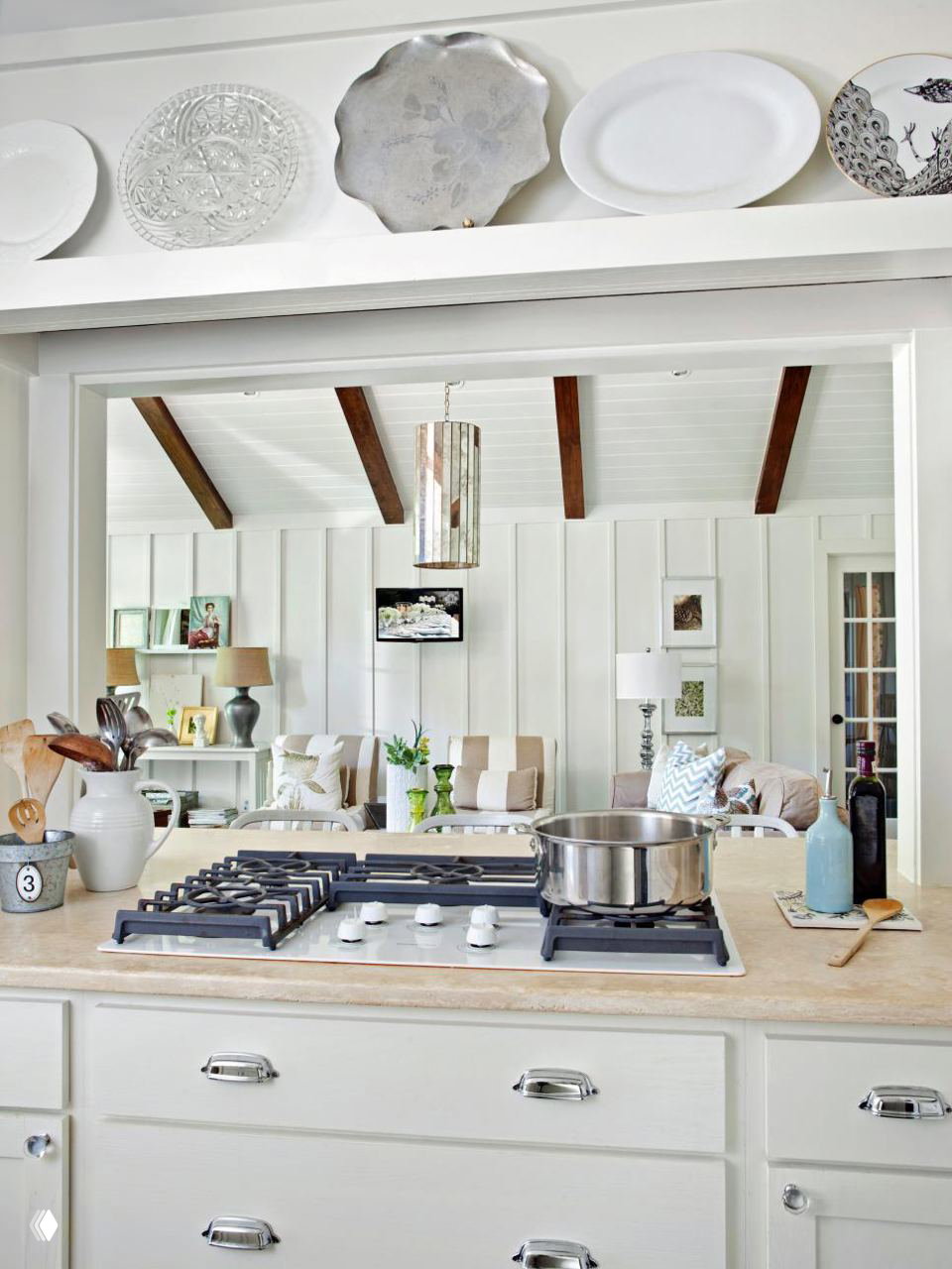 Кухонная столешница с варочной панелью на переднем плане и широким проёмом в гостиную — пример объединённой зоны через окно‑проём