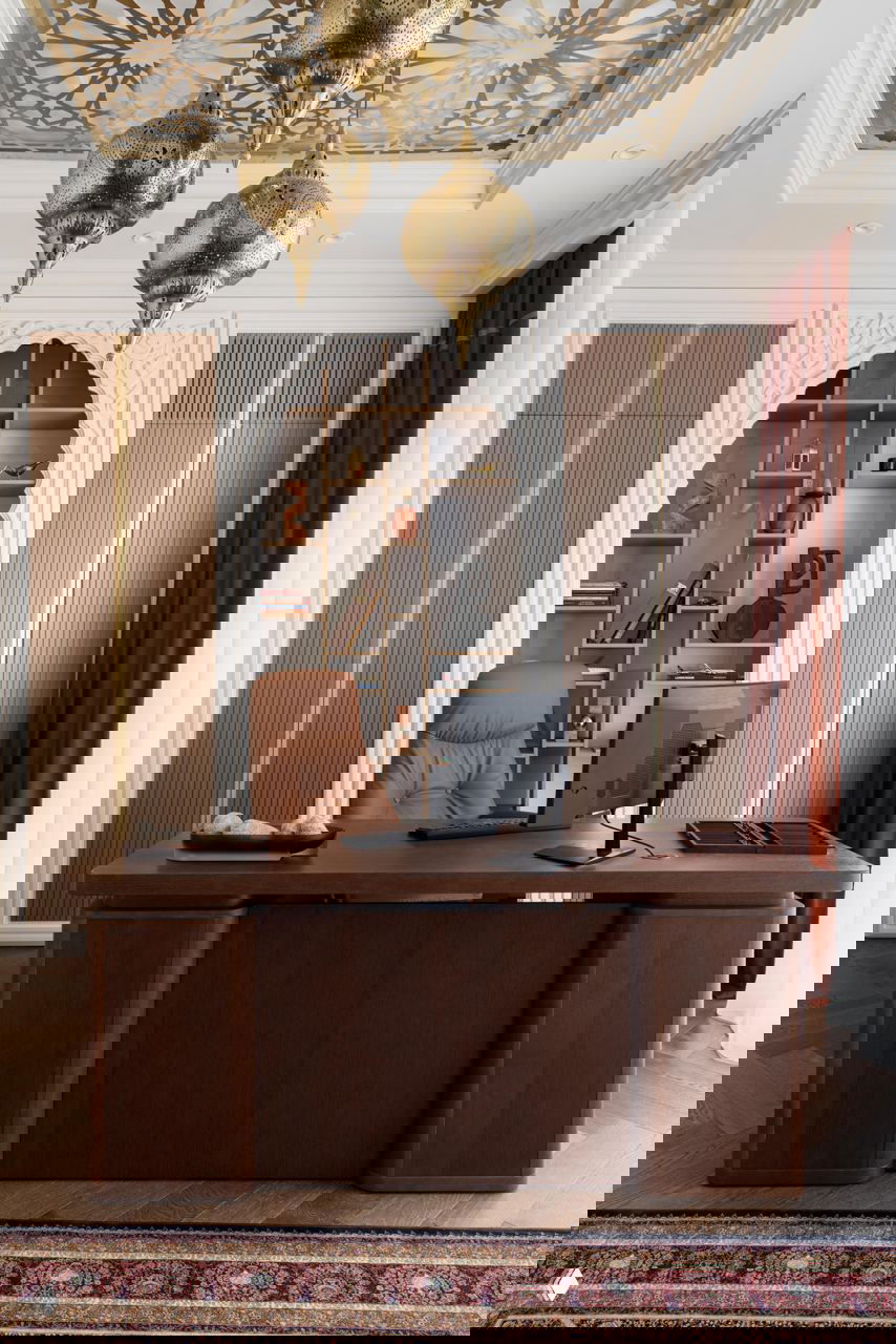 Рабочий кабинет с деревянным столом, резной аркой-решёткой, декоративными латунными светильниками в марокканском стиле и книжными полками.