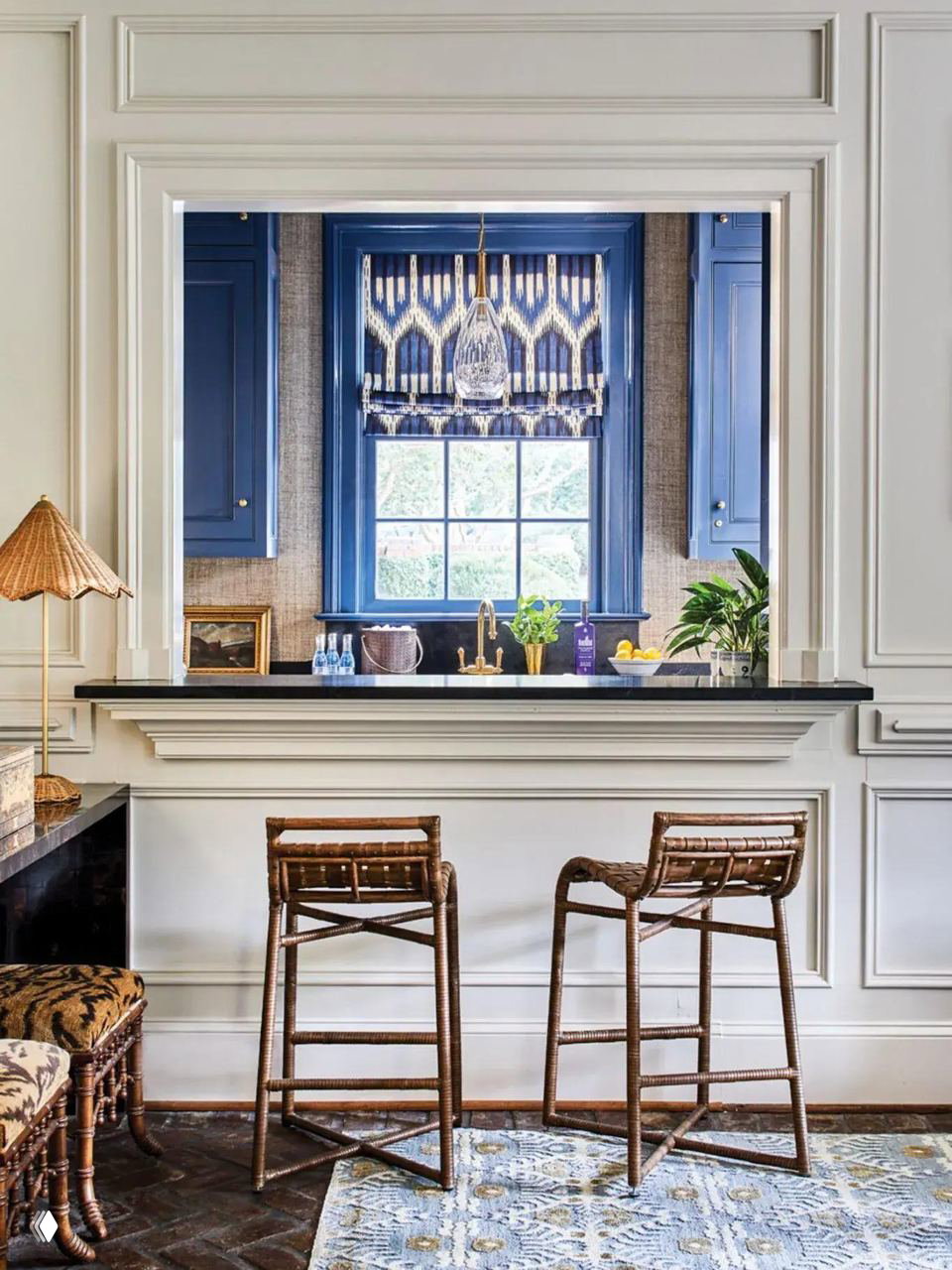 Классический интерьер с оформленным проёмом: тёмно‑синие шкафы вокруг окна и пара плетёных барных стульев у барной стойки