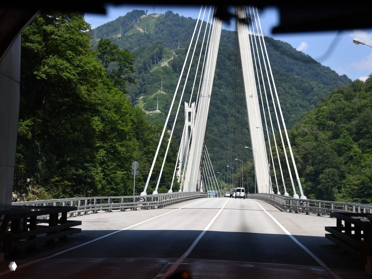 Современный виадукт через горную долину с подвесными опорами и полосами движения, вид с проезжей части на мост и лесистые склоны.