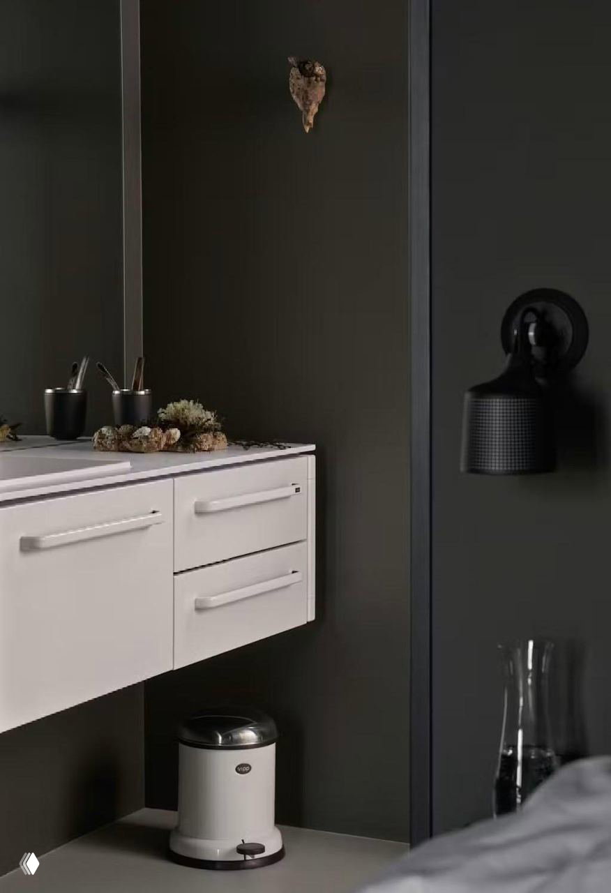 Фрагмент ванной/туалетного уголка: белая тумба, настенный светильник и компактный функциональный интерьер в контрастных тёмных тонах.
