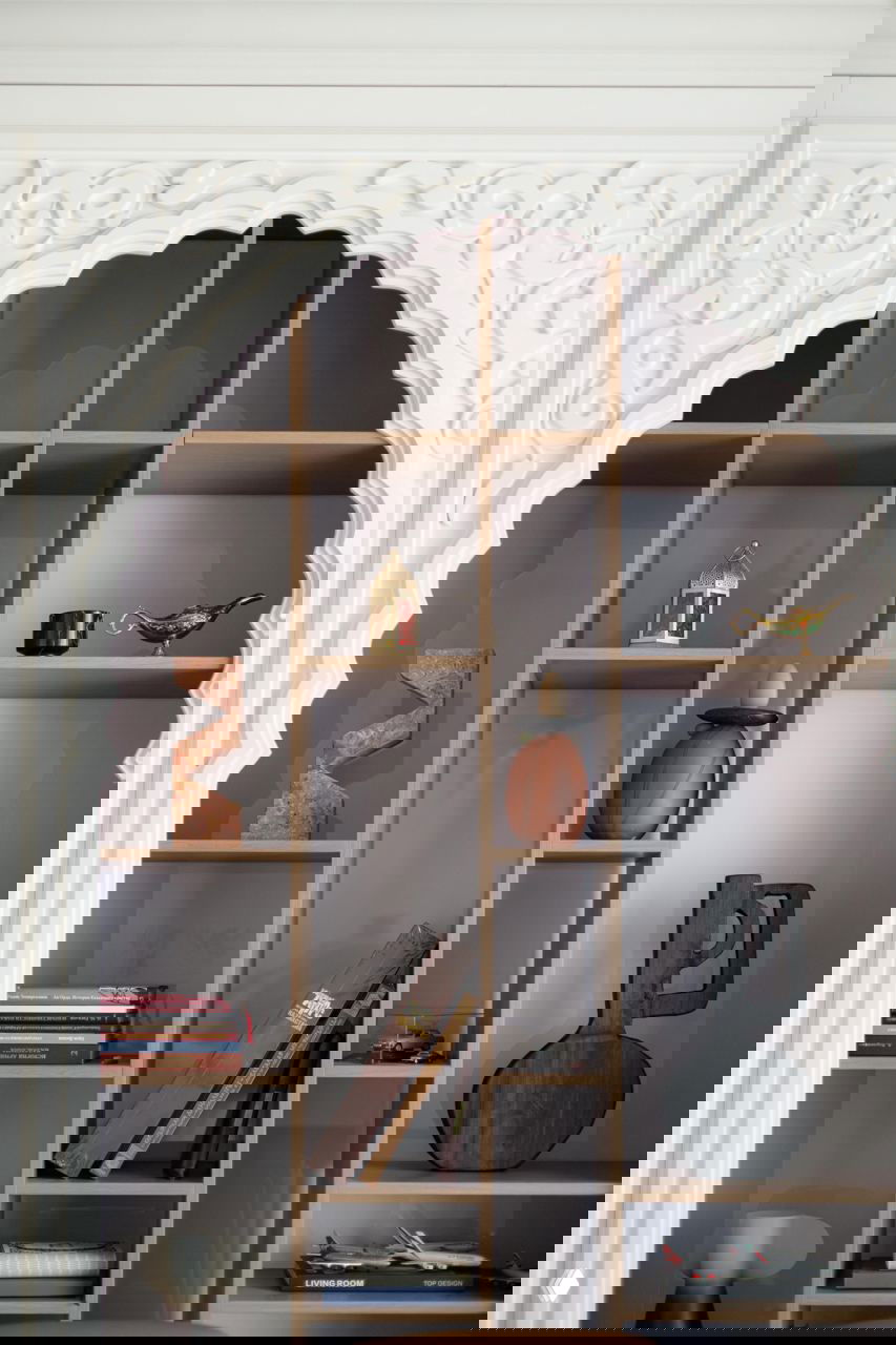 Крупный план декоративной ниши и полок с аксессуарами и книгами, стилистика сочетает современную мебель и восточные декоративные элементы.