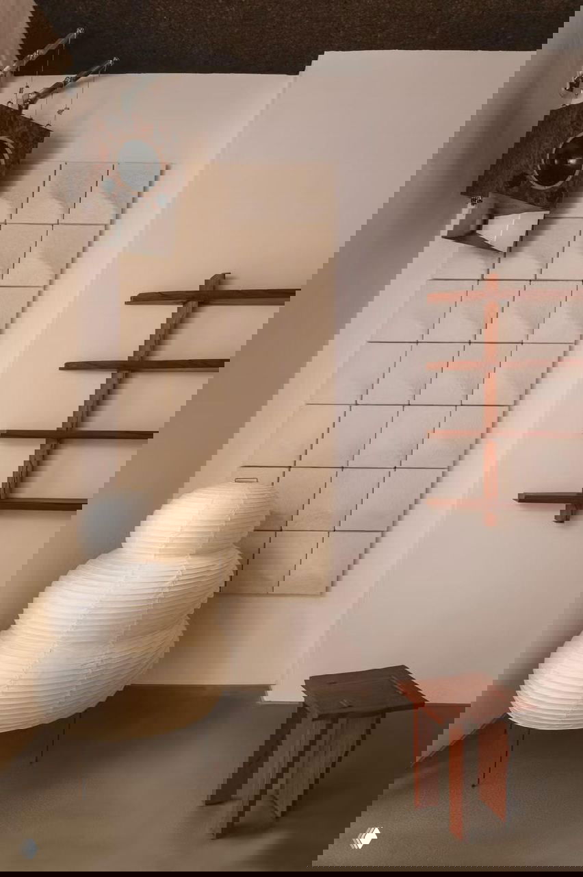 Акцентный угол с акустическими панелями и подвесным динамиком, рядом декоративный бумажный торшер в форме слоёной скульптуры и минималистичная полка.